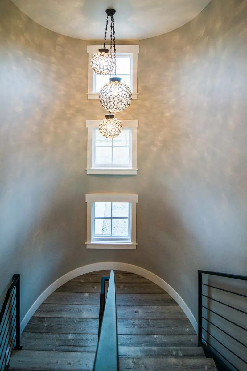 Curved stair landing with tall windows, globe pendants, and wood treads with black metal railing