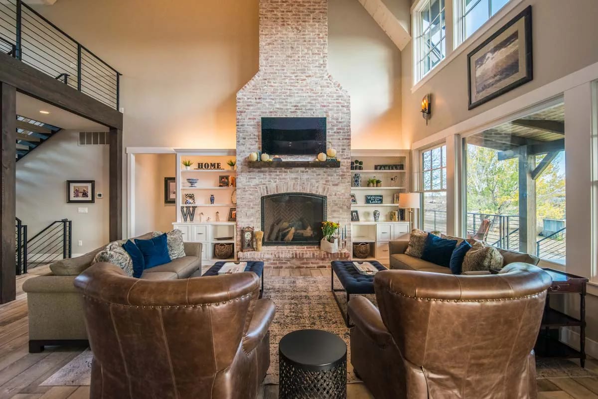Double-height great room with brick fireplace, built-ins, and large windows overlooking deck