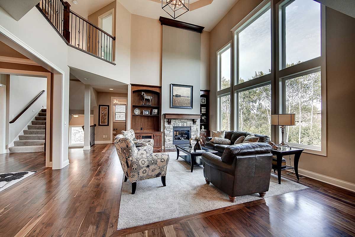 Double-height living room with large windows, stone fireplace, and warm wood flooring