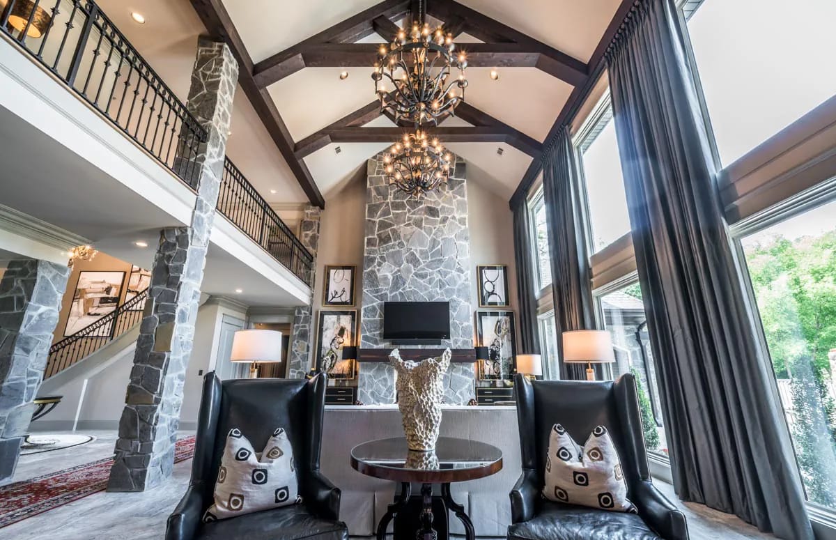 Dramatic great room with stone fireplace, vaulted ceiling, timber beams, and expansive windows