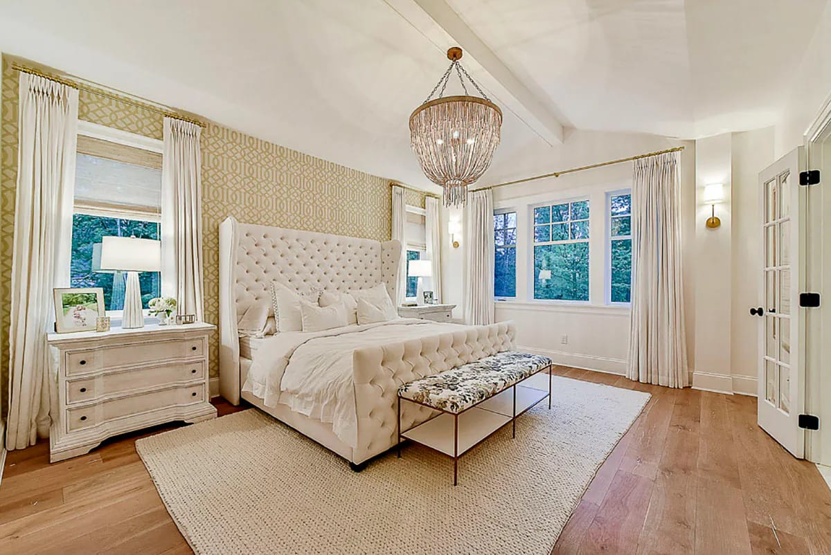 Elegant bedroom with tufted bed, crystal chandelier, and vaulted ceiling with exposed beams