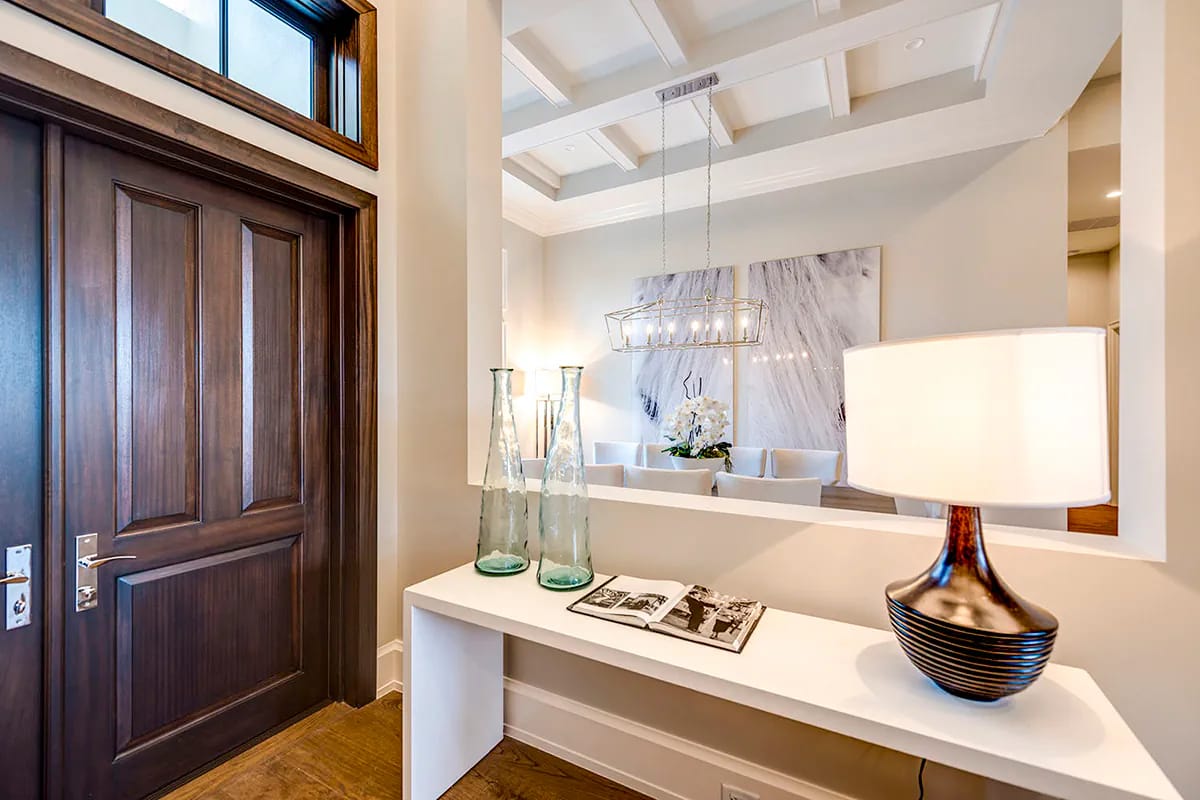 Elegant foyer with dark wood door, white console, coffered ceiling, chandelier, and adjacent seating area