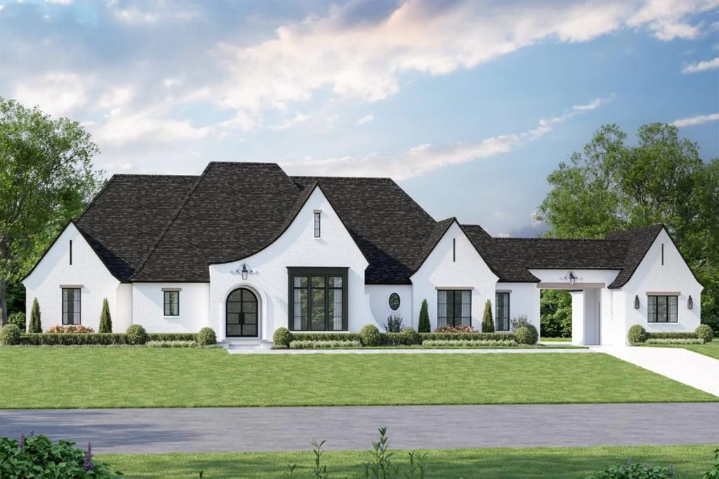 Elegant white brick home with steep gabled roof, arched entry, and porte-cochère in a manicured landscape.