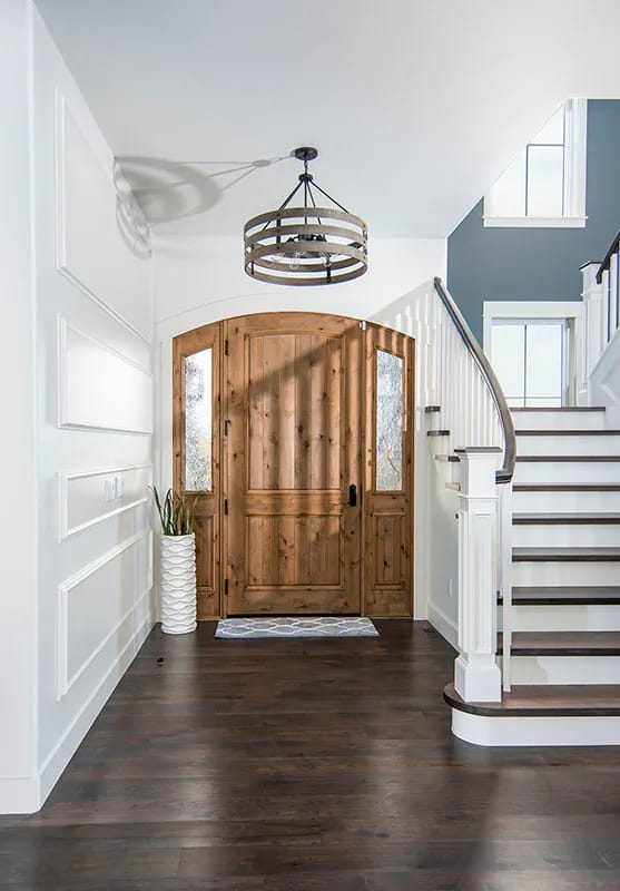 Entry foyer with arched wood door, white trim, sweeping staircase, and dark wood flooring
