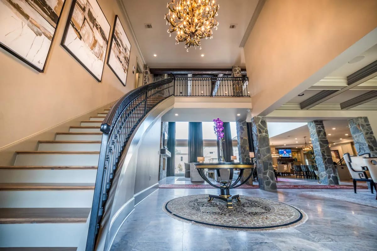 Grand foyer with curved staircase, chandelier, stone columns, and marble flooring