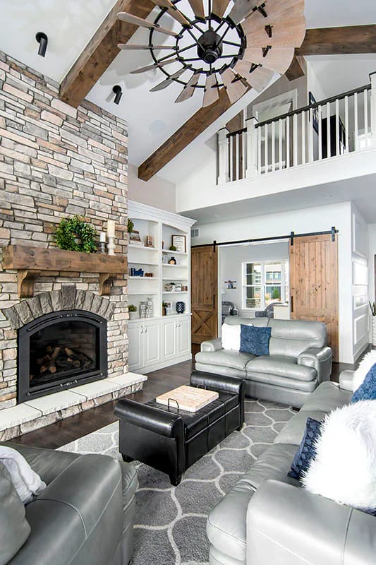 Great room with stone fireplace, vaulted ceiling with wood beams, and rustic barn doors