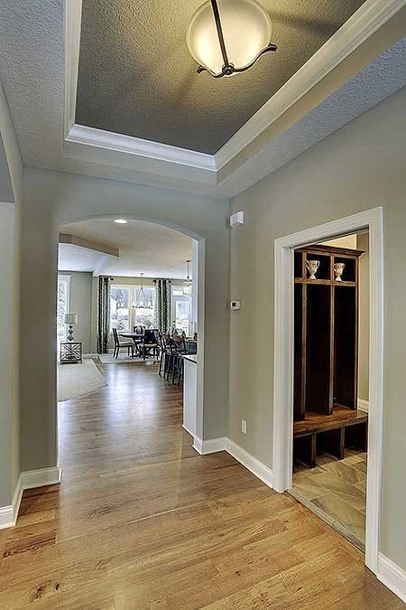 Hallway with tray ceiling, hardwood floors, and built-in mudroom bench leading to open living space