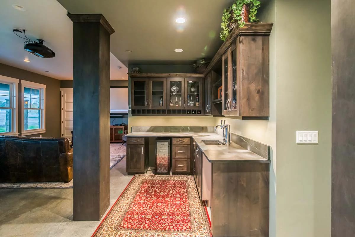 Home bar with dark wood cabinets, stone-look countertops, and red rug in open living space