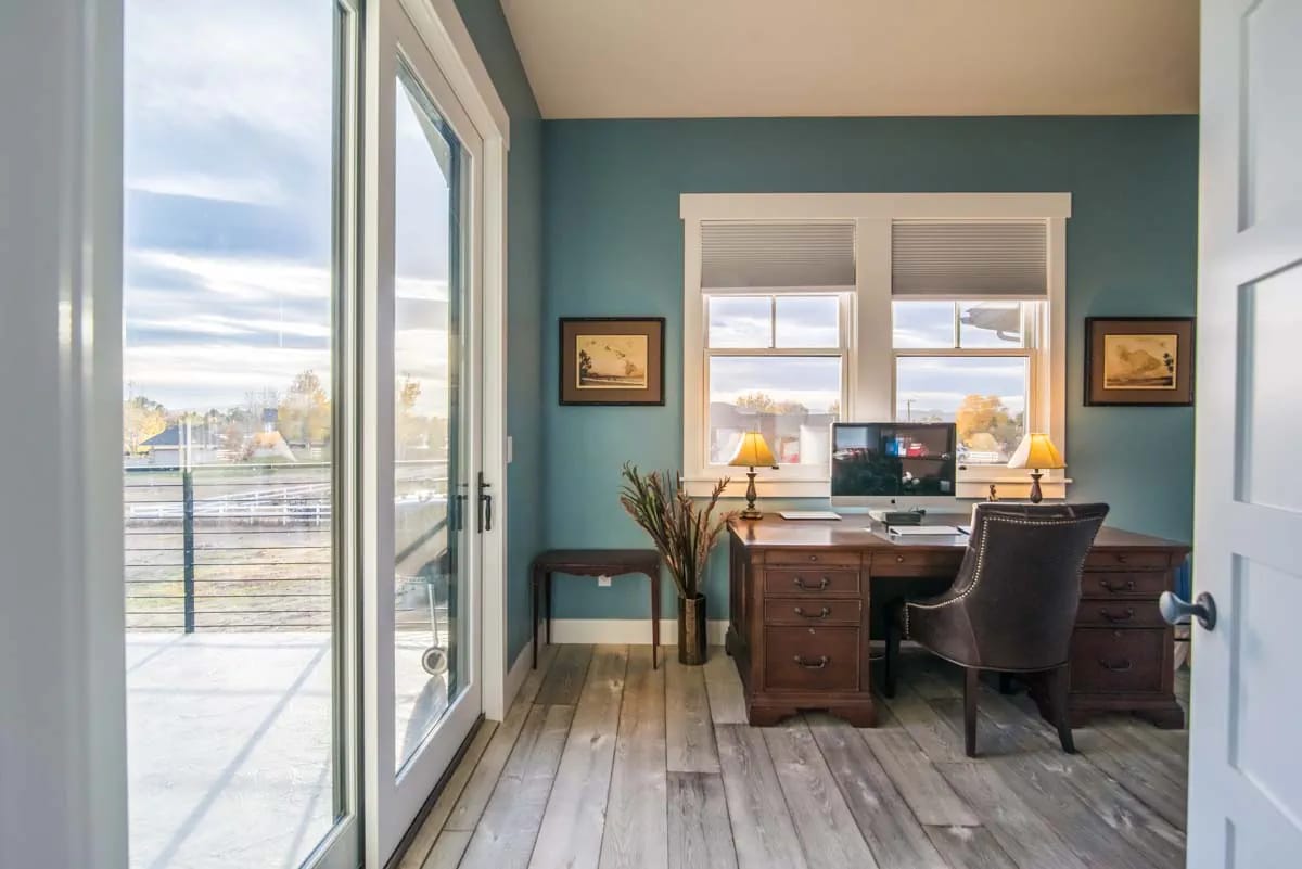 Home office with blue walls, wood desk, large windows, and glass doors to a balcony