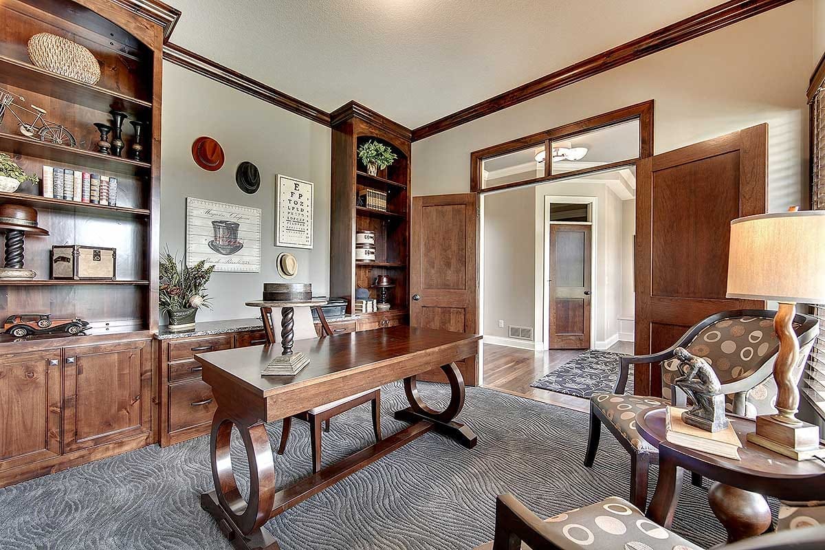 Home office with dark wood built-ins, central desk, and patterned carpet