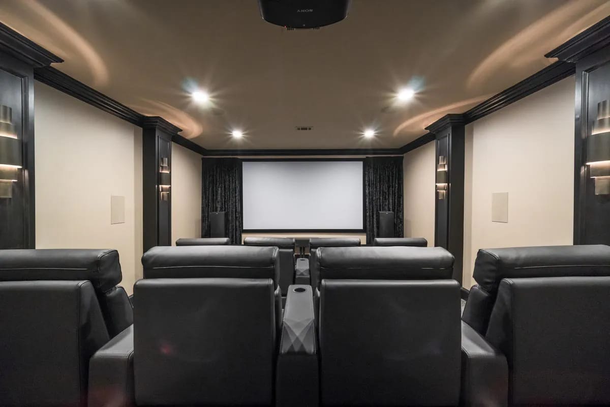 Home theater room with tiered leather recliners, large screen, and dark wood trim