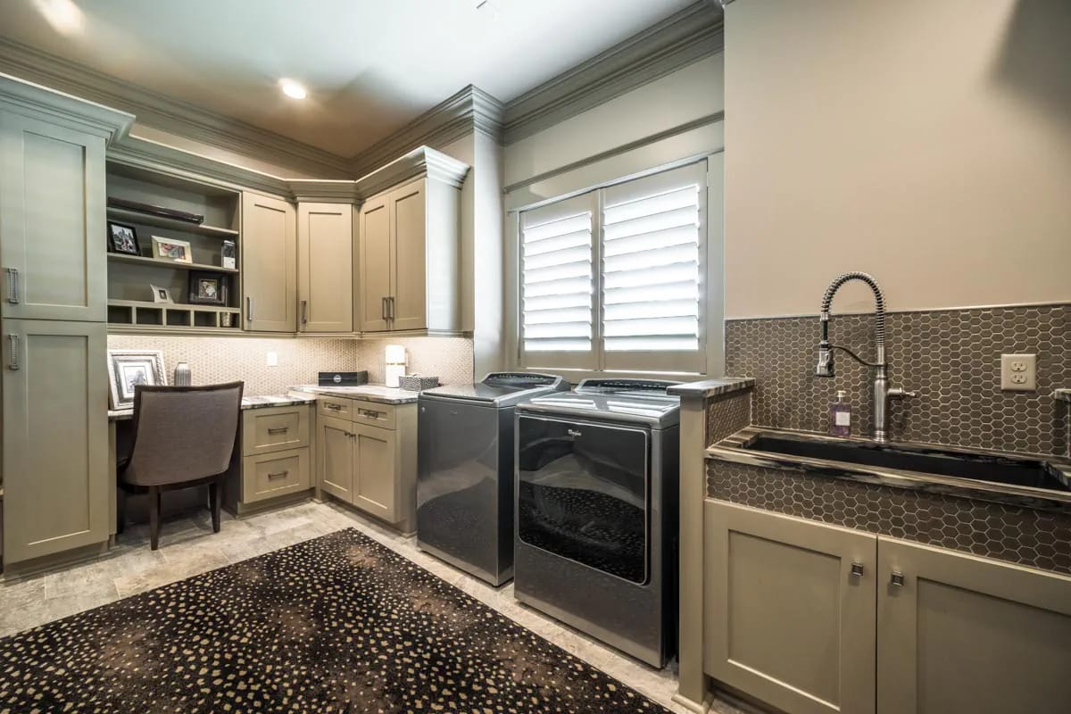 Laundry room with built-in desk, taupe cabinetry, front-load washer and dryer, and hex tile backsplash
