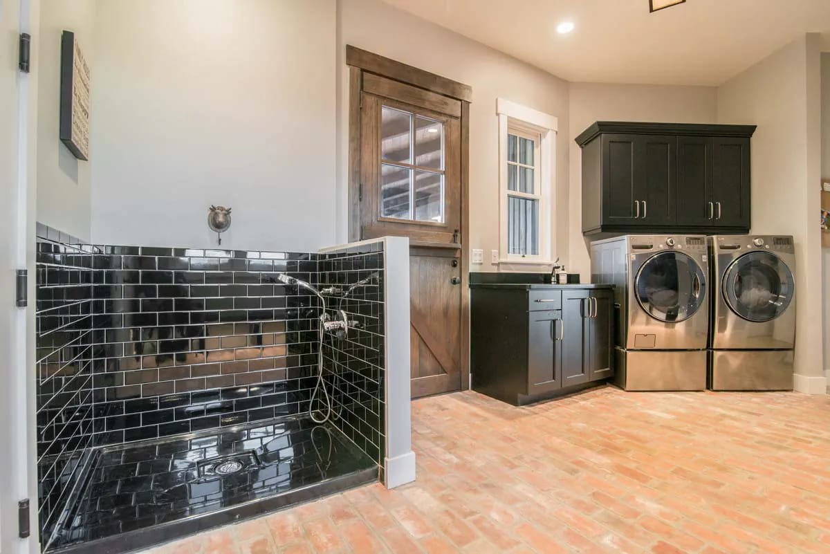 Laundry room with dog wash, black cabinetry, brick floor, and stainless washer and dryer