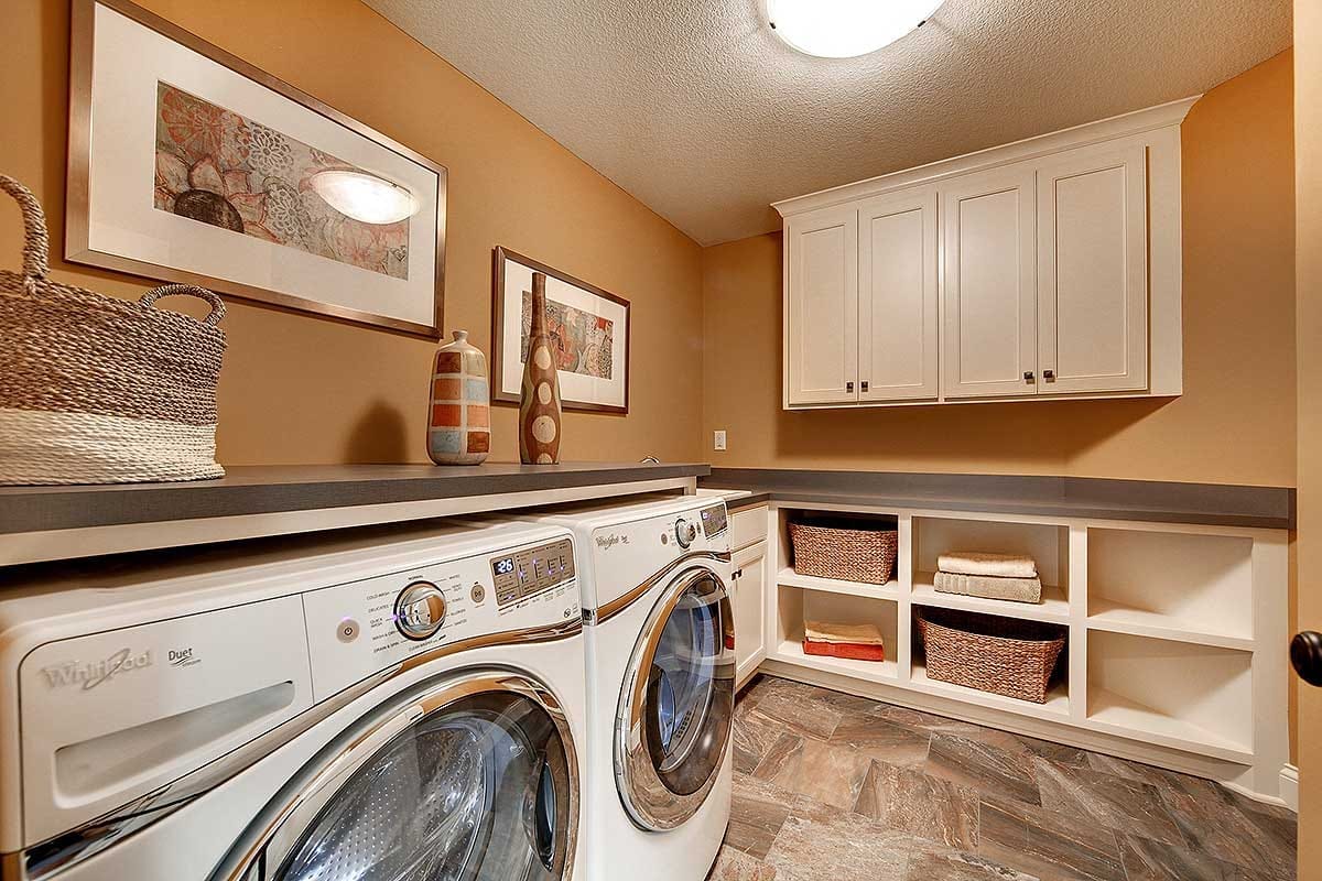 Laundry room with front-load washer and dryer, shaker cabinets, and open shelving with baskets