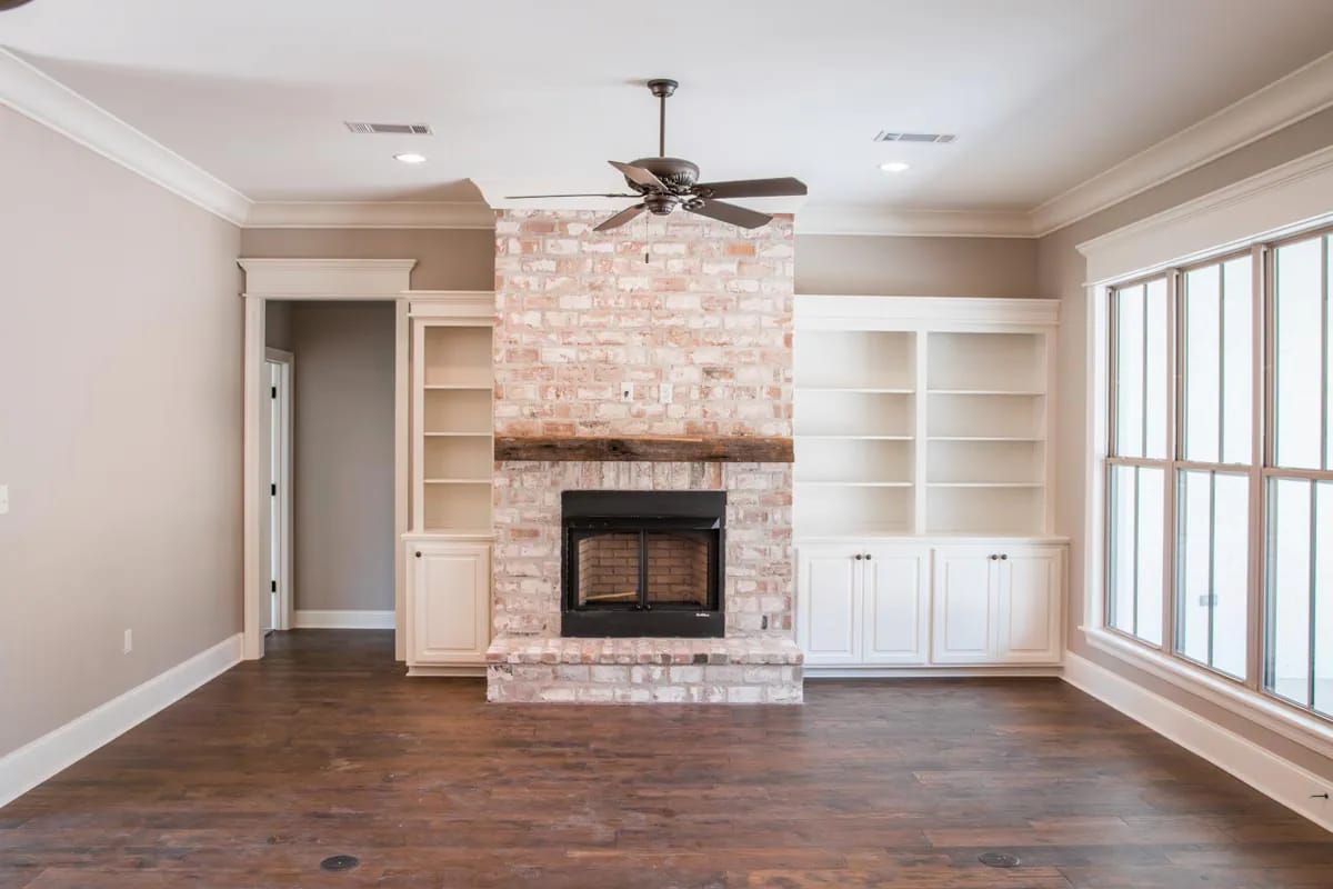 Living room with painted brick fireplace, white built-ins, dark wood flooring, and large divided-light windows