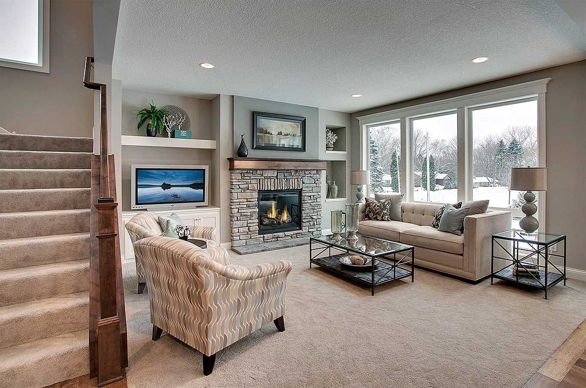 Living room with stone fireplace, large windows, and neutral modern furnishings