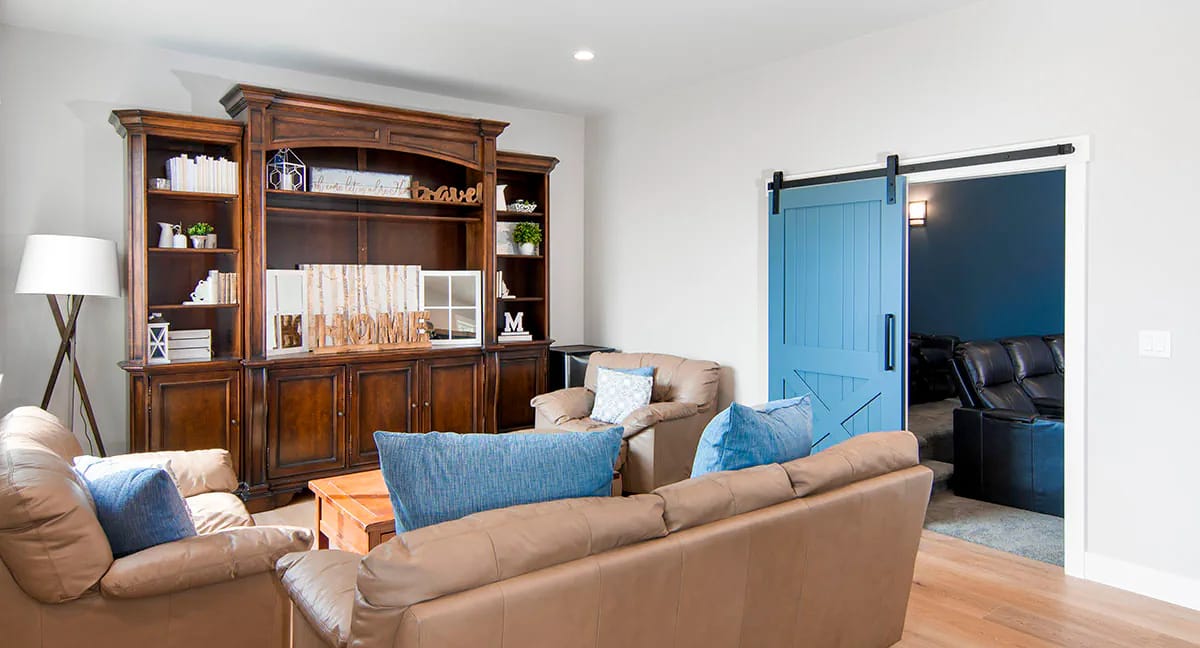 Living room with tan sofas, dark wood shelves, and blue barn door leading to adjacent room