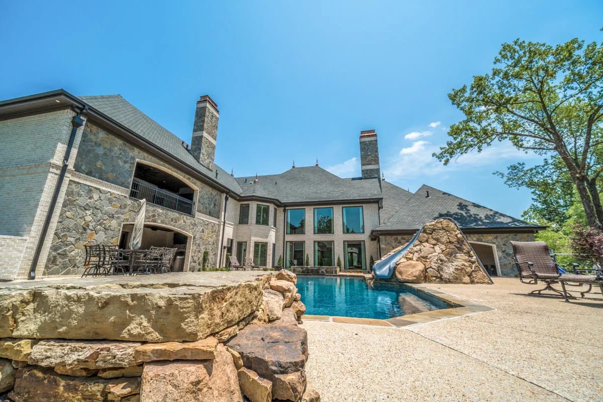 Luxurious home exterior with stone and brick facade overlooking a pool and waterslide.