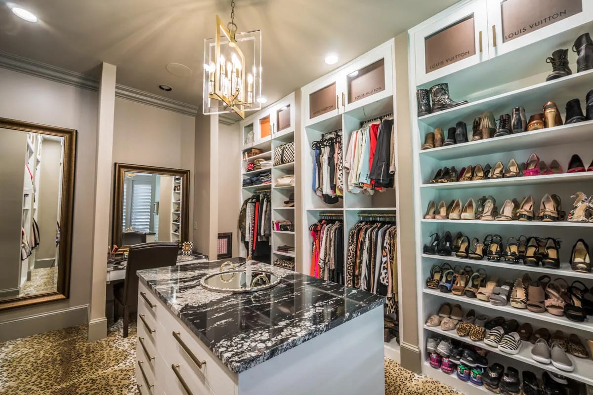 Luxurious walk-in closet with marble island, open shelving, and gold chandelier