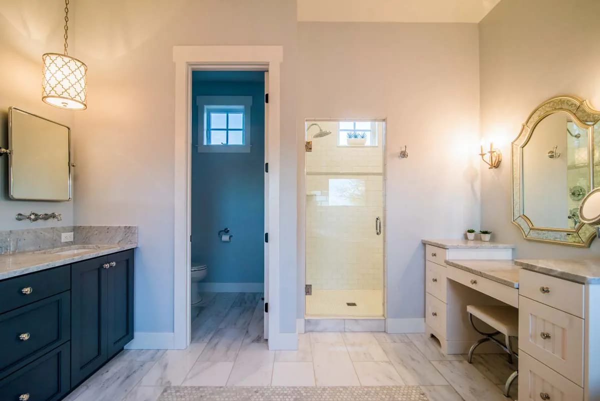 Luxury bathroom with navy and white vanities, marble counters, glass shower, and makeup station