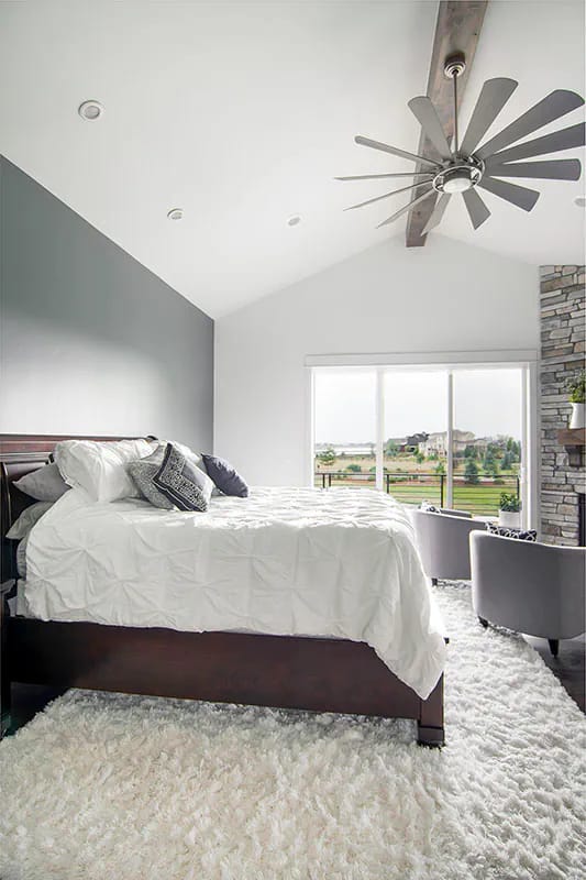 Modern bedroom with vaulted ceiling, large window, and stone fireplace