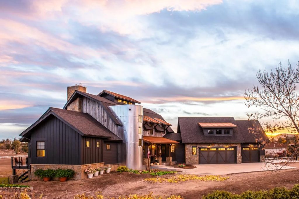 Modern farmhouse exterior with dark siding, stone accents, and a metal silo at sunset