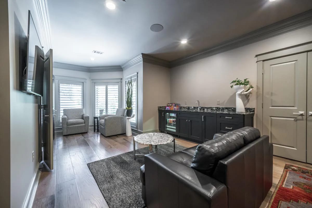 Modern lounge with black sofa, wet bar, armchairs, and large windows with plantation shutters