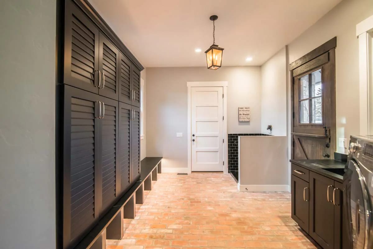 Mudroom with dark built-in lockers, brick floor, and farmhouse-style wooden Dutch door