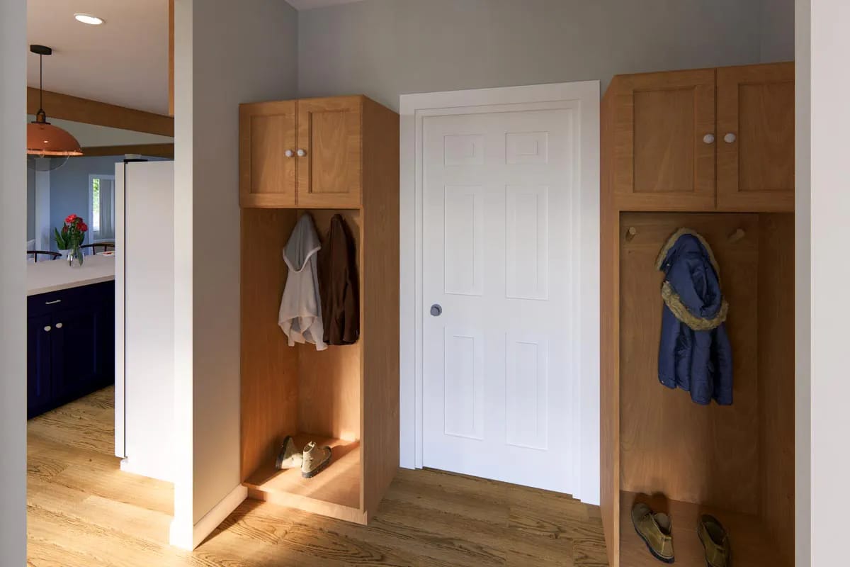 Mudroom with oak built-ins, coat hooks, shoe storage, and a white paneled door