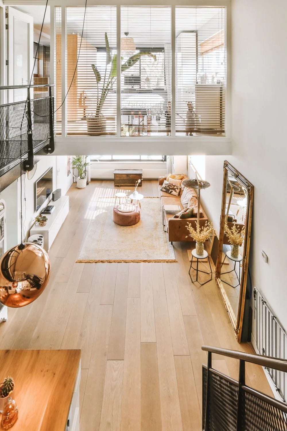 Long, narrow great room in a narrow lot house plan, featuring a living area with a sofa, coffee table, rug, large windows with blinds, and a visible upper-level railing