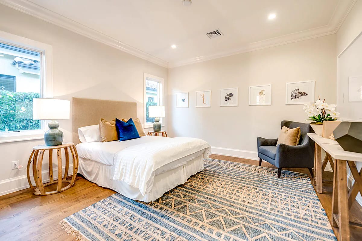 Neutral bedroom with upholstered bed, blue accents, wood floors, patterned rug, and framed artwork