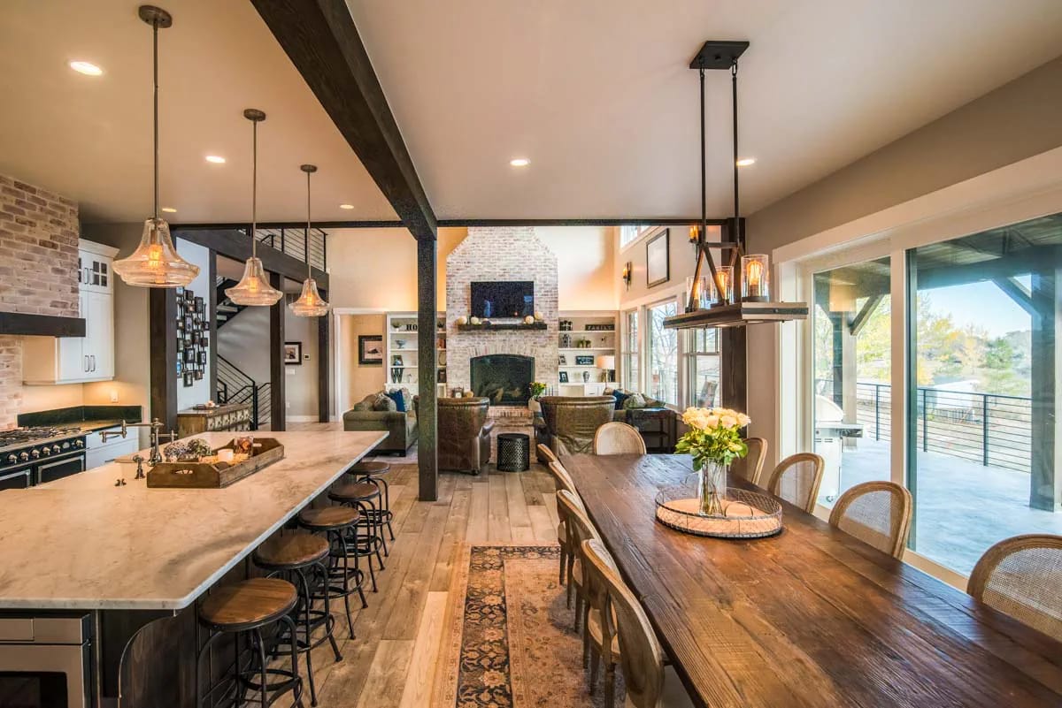 Open-concept kitchen, dining, and living area with rustic finishes and large windows