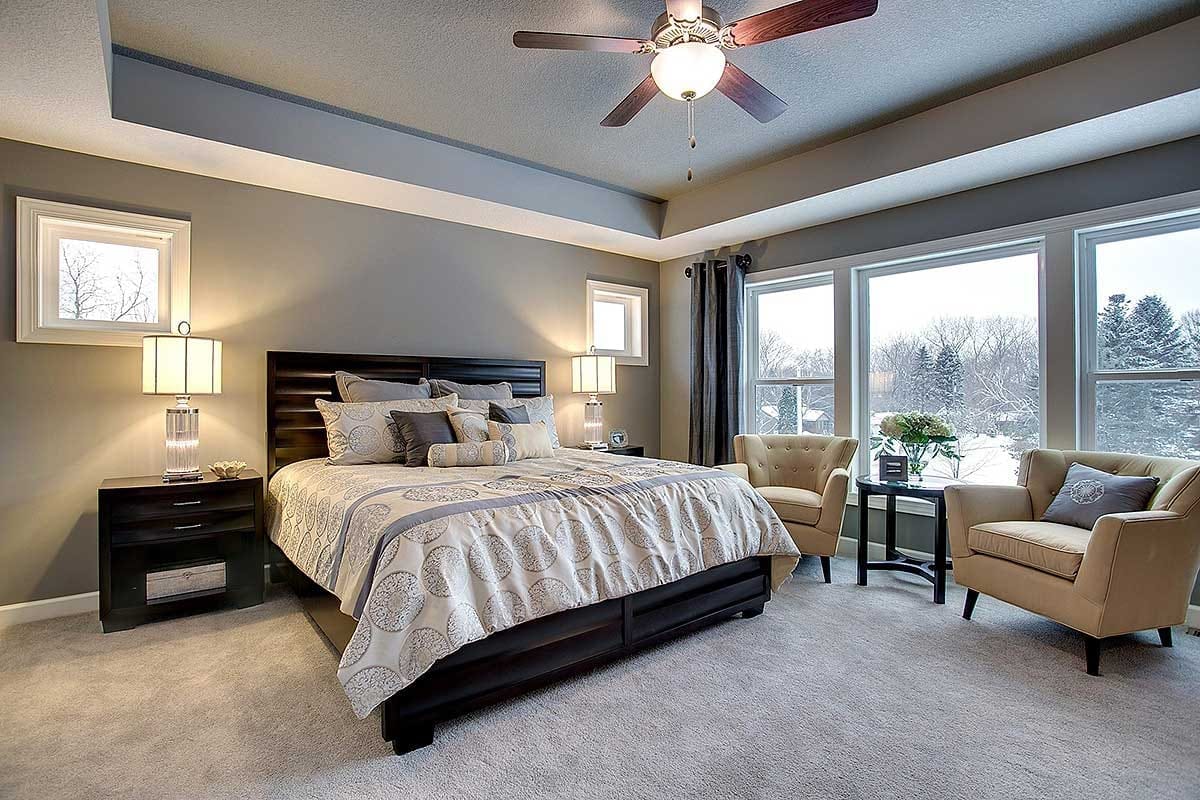 Primary bedroom with tray ceiling, large windows, and neutral contemporary furnishings