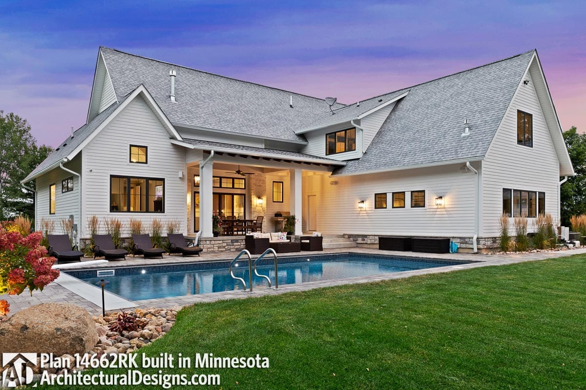 Rear exterior of a light-sided home with gabled roofs, covered patio, stone fireplace, and swimming pool
