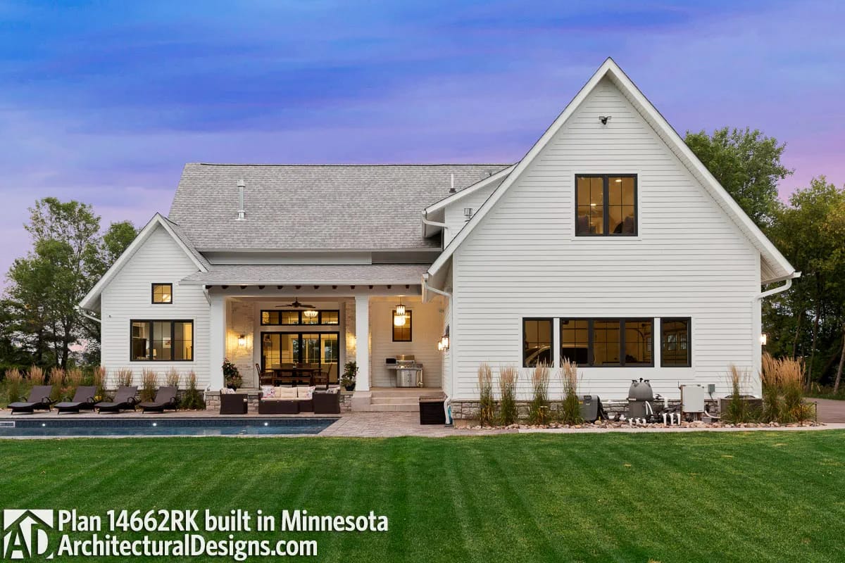 Rear exterior of a white gabled home with covered patio, pool, lounge seating, and landscaped lawn