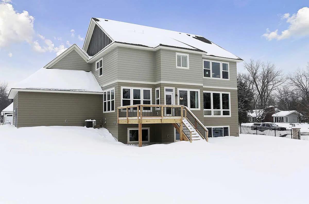 Rear exterior view of a two-story home with large windows, deck, and snow-covered yard.