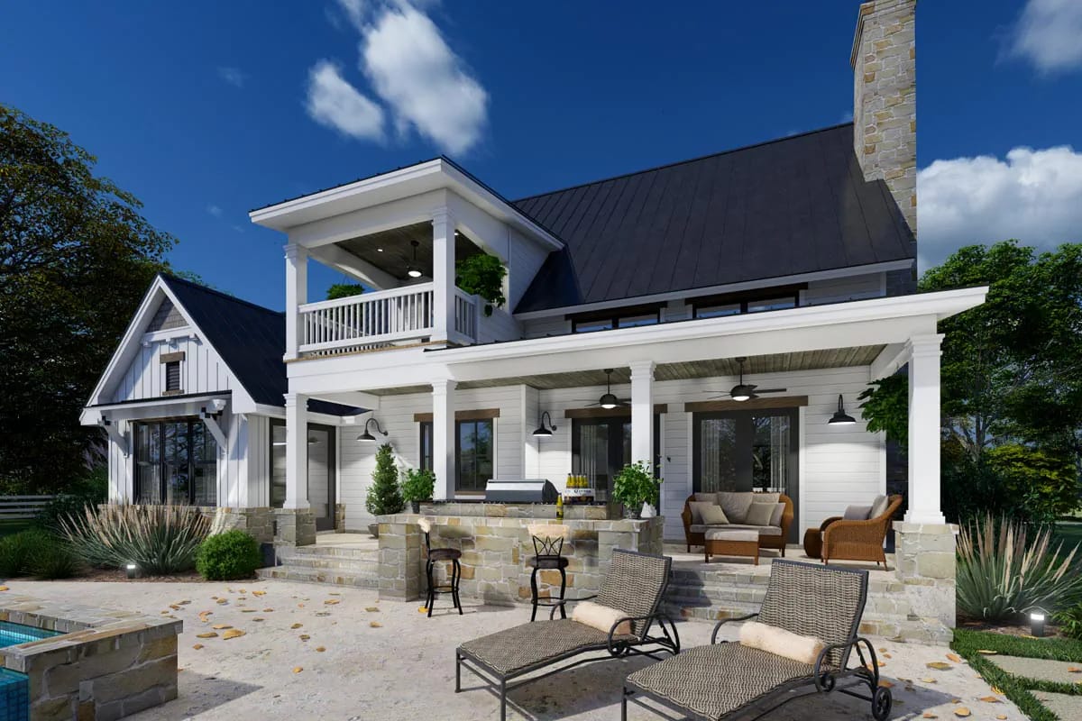 Rear exterior with white siding, dark roofs, upper balcony, covered porch, stone terrace, and outdoor seating