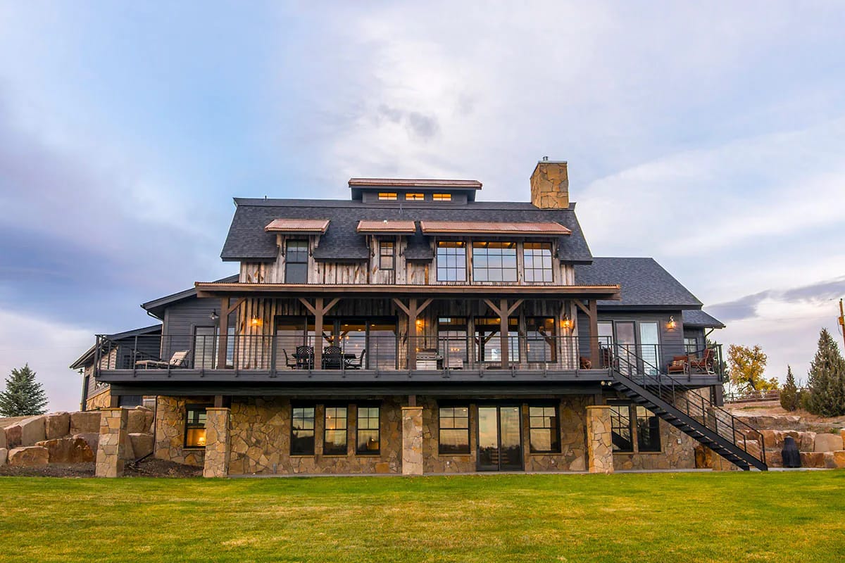 Rustic mountain-style home with large covered deck, stone base, and extensive windows on the rear facade.