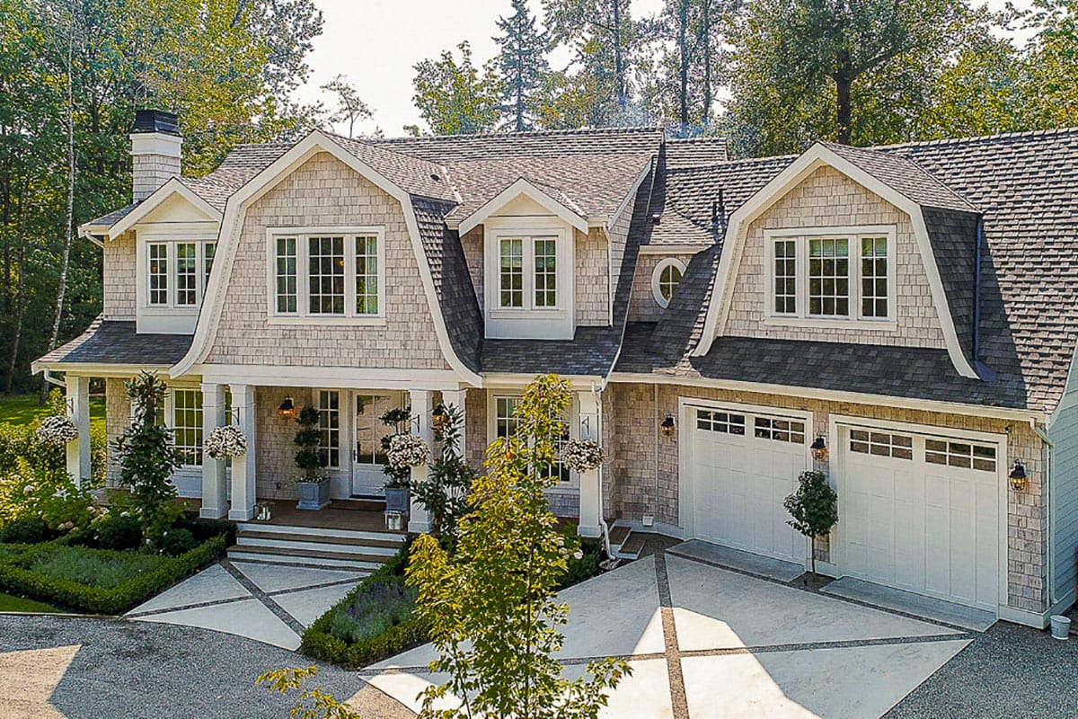 Shingle-style house with flared gables, front porch, and double garage in a landscaped setting