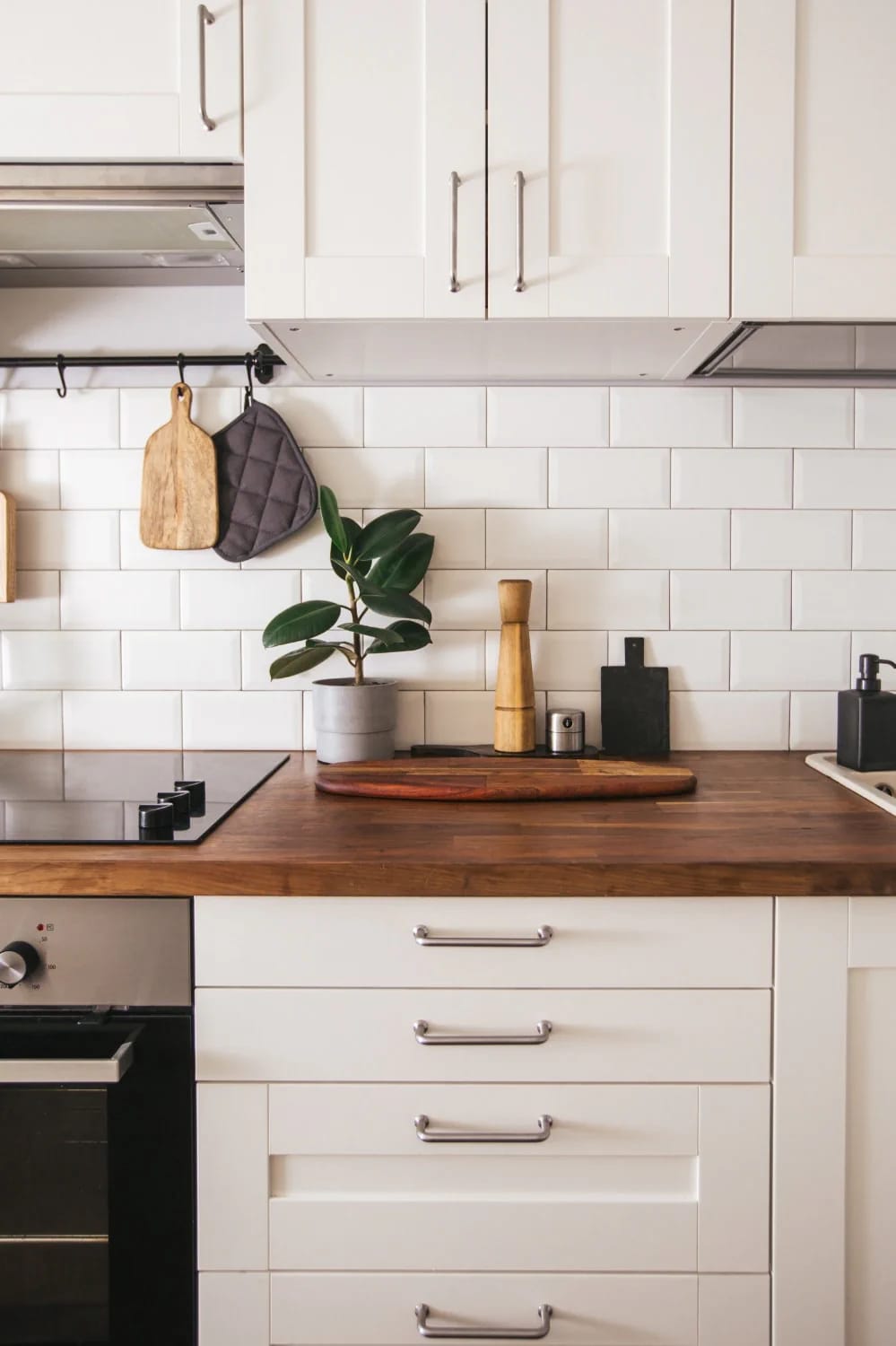 Small Apartment Kitchen Countertop Ideas Small apartment kitchen with white cabinets, a wood countertop, white subway tile backsplash, hanging utensils, potted plant, cutting boards, cooktop, and drawers