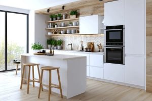 11 Small Apartment Kitchen Ideas That Give You Back Your Counter 7 Bright small apartment kitchen with a white island, two wooden stools, open shelves displaying dishes and plants, white cabinets, built-in ovens, and a tiled backsplash