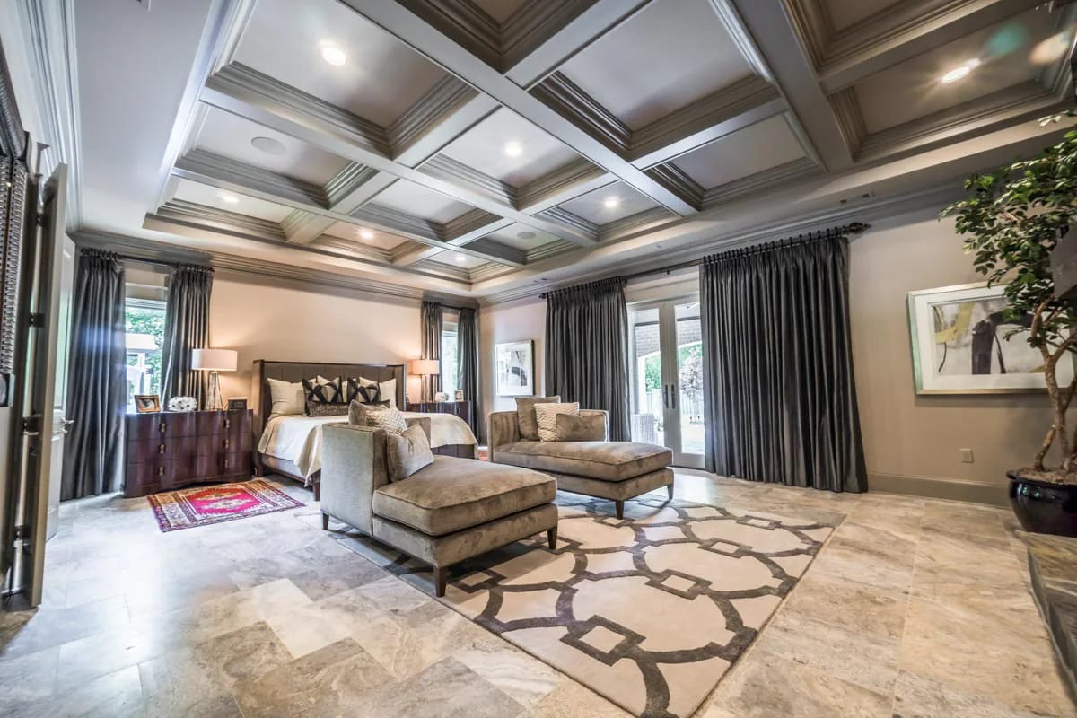Spacious bedroom with coffered ceiling, marble-look floor, French doors, and plush chaise lounges.