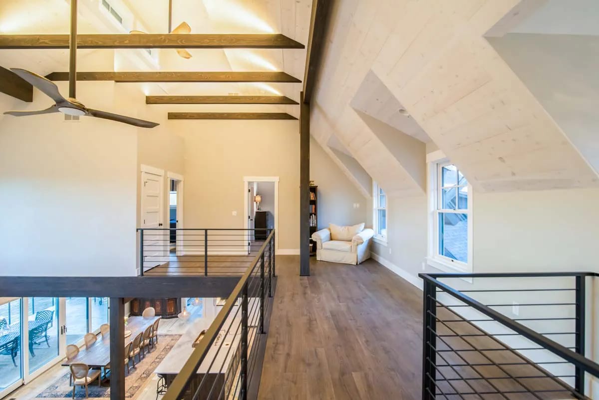 Spacious loft with vaulted ceiling, exposed beams, wood floors, and metal railing overlooking dining area