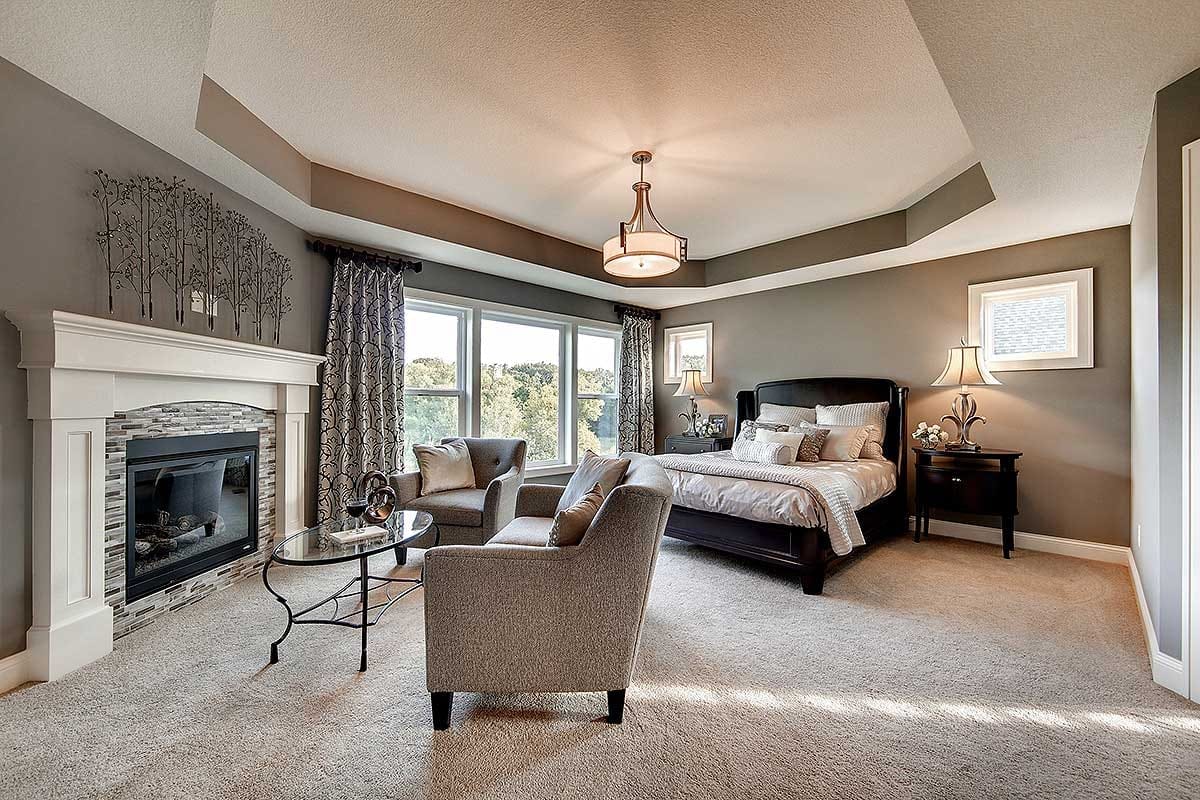 Spacious primary bedroom with tray ceiling, fireplace, large windows, and elegant furnishings