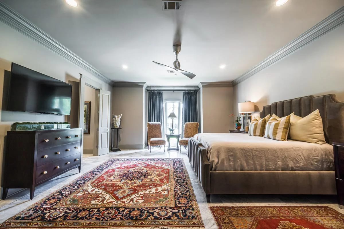Spacious primary bedroom with tufted bed, oriental rug, and elegant traditional detailing