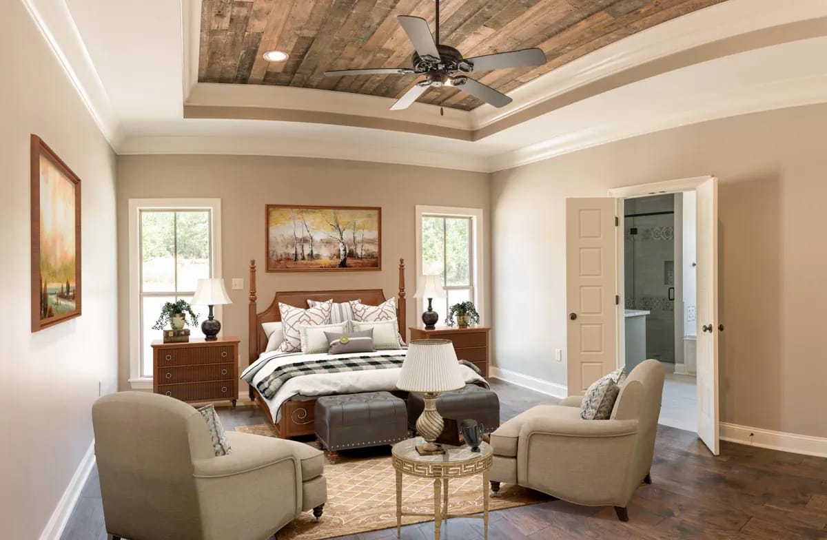 Staged bedroom with wood-plank tray ceiling, four-poster bed, lounge chairs, and adjoining bathroom