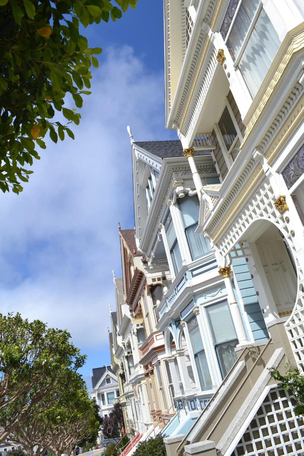 Row of ornate Victorian homes with white, pale blue, and muted red exterior details beneath a blue sky, illustrating a balanced three-color Victorian paint scheme