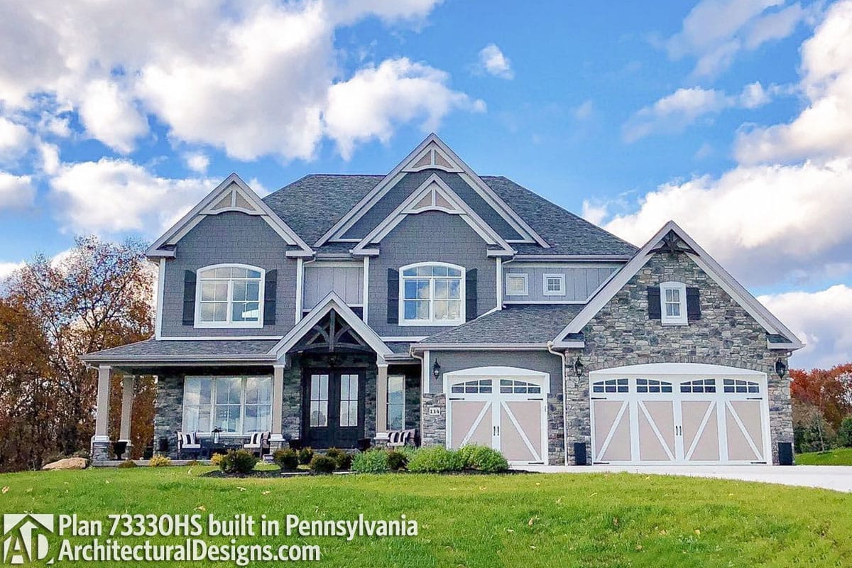 Two-story home with stone and gray siding, triple gables, arched windows, and a three-car garage.