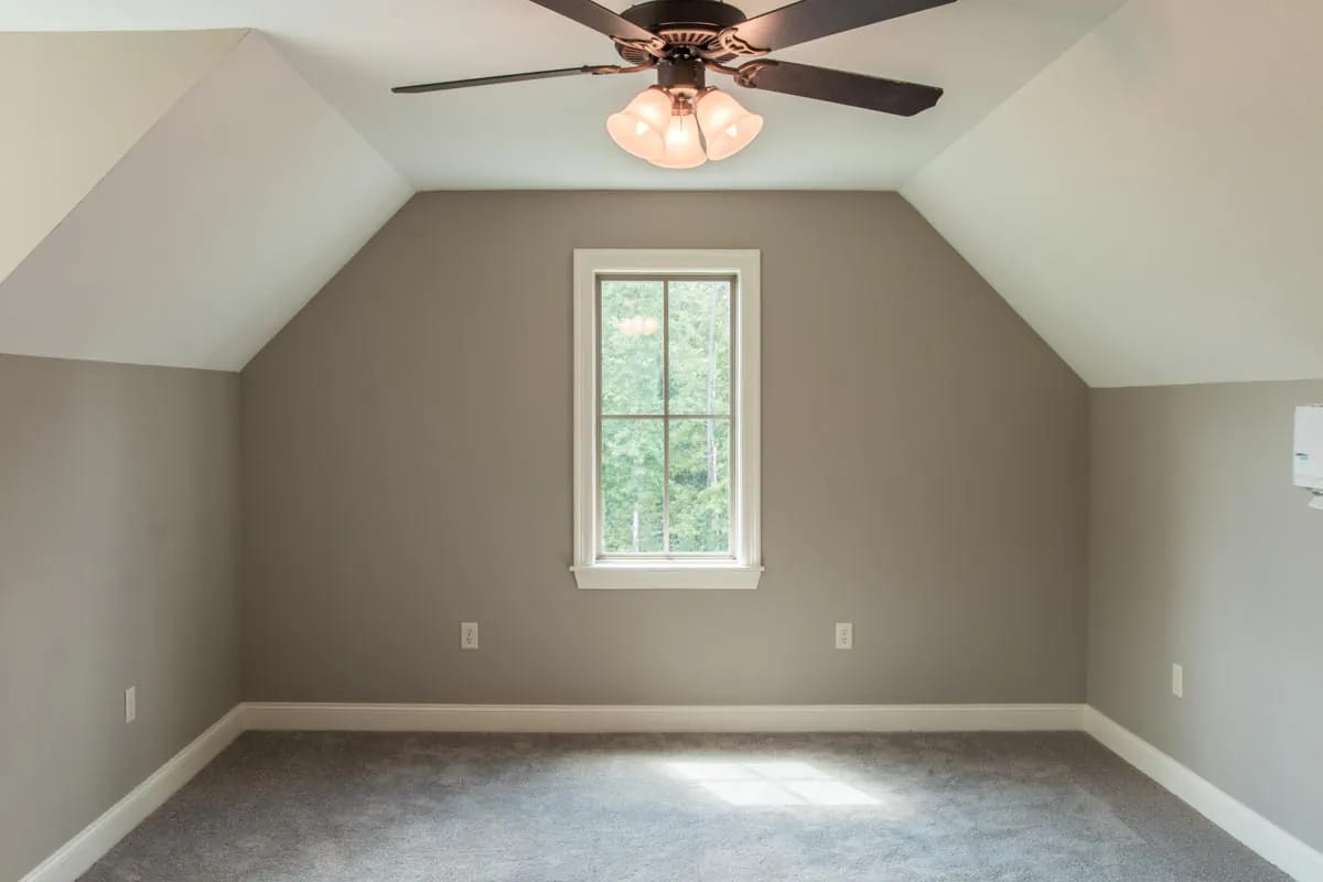 Unfurnished taupe room with sloped ceiling, centered window, gray carpet, and dark ceiling fan