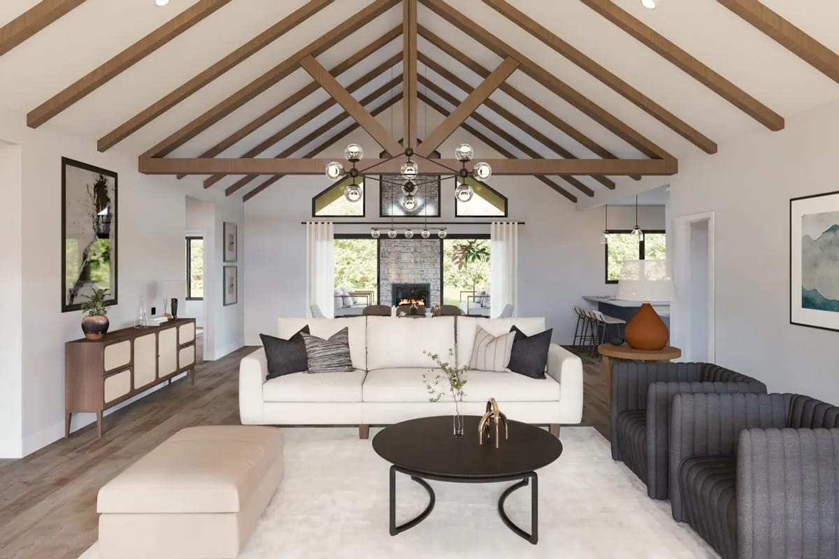 Vaulted living room with exposed wood beams, stone fireplace, contemporary seating, and an adjoining kitchen